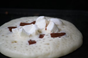 Sprinkle chocolate chips and marshmallows onto pancakes.